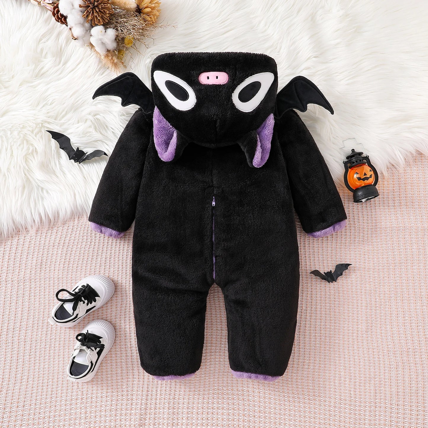 Black bat-themed baby onesie with shoes on a soft surface