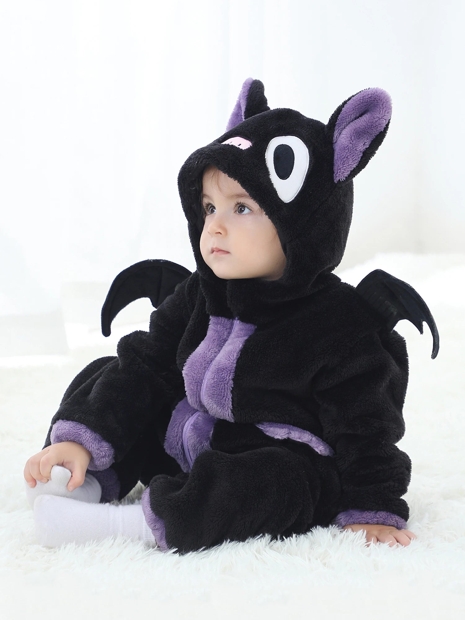 Baby in a black and purple dragon costume sitting on a white surface